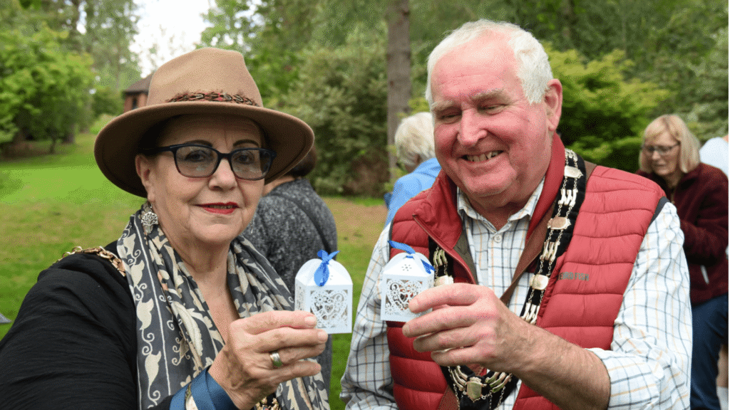 Two people wearing mayoral chains stand together holding a white decorative box with a butterfly inside.