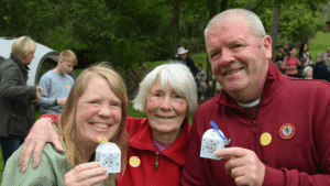 three people stand together arem in arm which holding decorative boxes with a butterfly inside