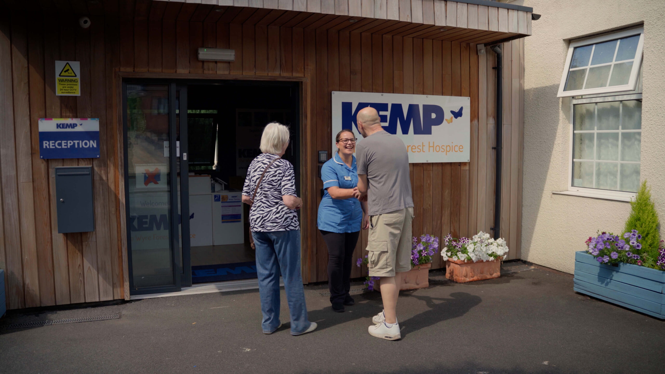 a womand and a gentleman are greeted at kemp hospice by a nurse wearing blue scrubs